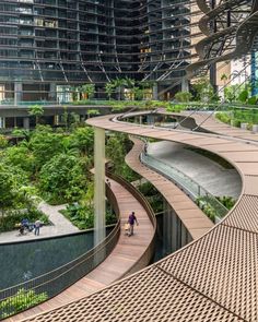 two people walking on a wooden walkway in the middle of a city with high rise buildings