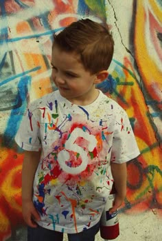 a young boy standing in front of graffiti covered wall