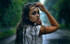 a woman with wet hair standing in the rain holding her head to her ear and looking off into the distance