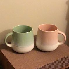 two coffee mugs sitting on top of a wooden table next to a white wall