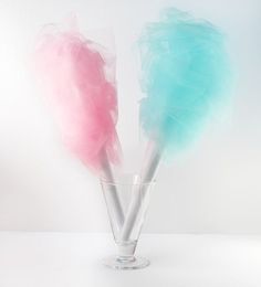 two lollipops are in a glass vase on a white surface, one is pink and the other is blue