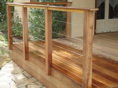 a wooden deck with metal railings next to a door and trees in the background