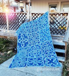 a blue quilt sitting on top of a wooden bench in front of a fenced yard