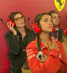 three women wearing red headphones and talking on cell phones in front of a ferrari logo