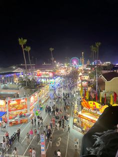 people are walking down the street in an amusement park at night with rides and food stalls