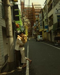 two people hugging each other on the side of an empty city street with buildings in the background