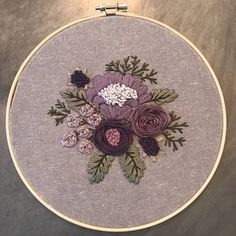 a close up of a embroidery on a wall hanging with flowers in the center and leaves around it