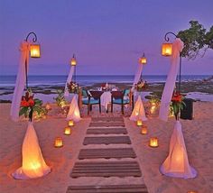 an outdoor wedding set up on the beach with candles and lanterns in front of it