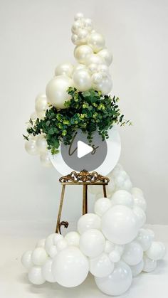 an arrangement of white balloons and greenery on a stand with a video player in the center