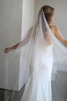 a woman in a white wedding dress with a veil on her head and hands behind her back