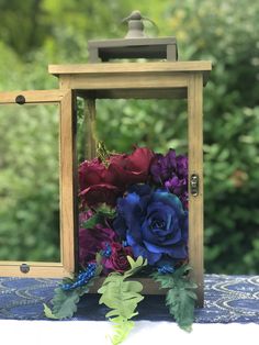 a flower arrangement in a wooden box on a table with blue and purple flowers around it