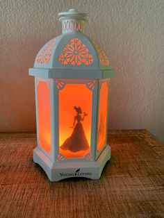 a small white lantern with a silhouette of a woman in a dress on it sitting on a wooden table