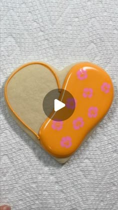 an orange heart shaped cookie with pink flowers on it and a video play button in the middle