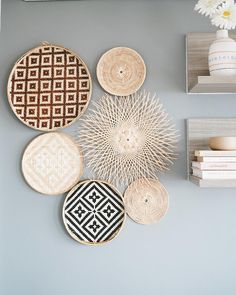 woven baskets are hanging on the wall above books and vases with flowers in them