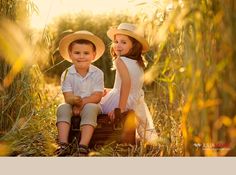 two children sitting on suitcases in the middle of tall grass with sun shining behind them