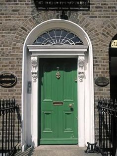 a green door is in front of a brick building with wrought iron fence around it