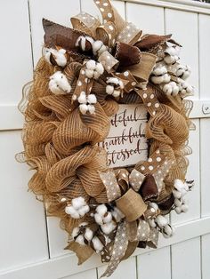 a wreath with cotton and burlocks hanging on the side of a white door