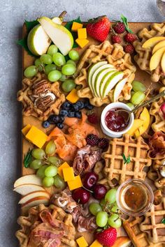 a wooden tray topped with waffles, apples, grapes and other food items