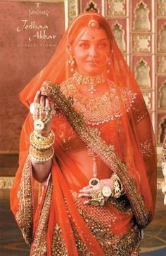 a woman in an orange bridal gown and jewelry is posing for the camera with her hand on her hip