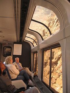 people sitting in seats on a train looking out the window at mountains and rocks outside