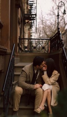 a man and woman are sitting on the steps together in front of some stairs, kissing