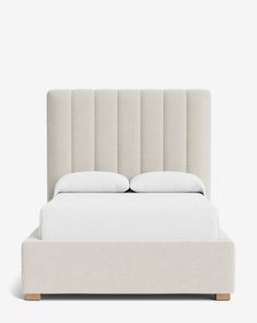 an upholstered bed with white sheets and pillows