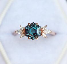 an emerald colored ring with three small white diamonds on the side and one blue diamond in the middle