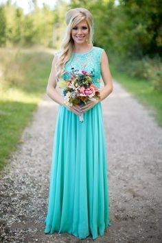 a woman in a long blue dress standing on a dirt road holding a bouquet of flowers