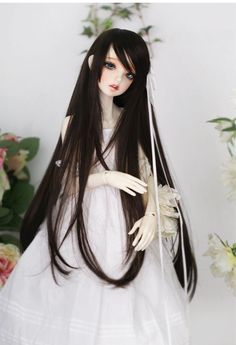 a doll with long black hair wearing a white dress and holding a flower in her hand