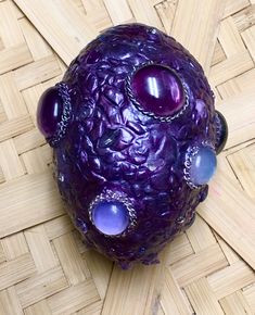 a purple vase sitting on top of a wooden floor next to a bamboo mat with beads