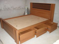 a wooden bed with drawers underneath it in a room that has no walls and concrete flooring