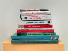 a stack of christmas books sitting on top of a yellow table next to a white wall