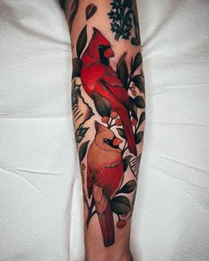 a red bird sitting on top of a tree branch next to leaves and berries tattoo