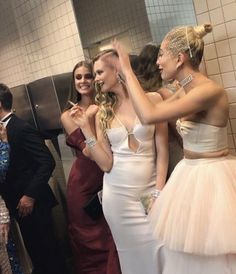 two women in white dresses are talking to each other while another woman is taking a selfie