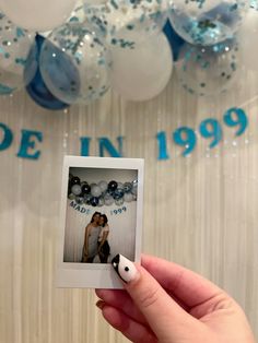 a person holding up a polaroid in front of balloons