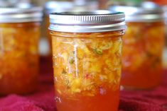 three jars filled with food sitting on top of a red table cloth next to each other