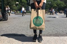 a woman standing on the street with a bag in her hand that says, who's foods?