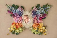 a baby in a butterfly costume surrounded by flowers and greenery on a tan background