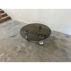 a glass and metal coffee table with three balls on it's bottom, sitting in front of some stairs