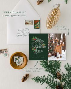 christmas cards and envelopes on top of a table with pine cones, evergreen leaves and other holiday decorations