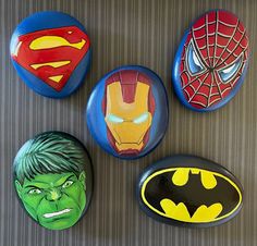 four painted rocks depicting superheros and the faces of batman, iron man, spider - man, and hulk - man