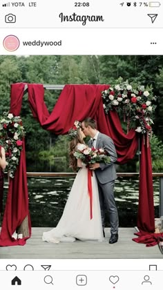 a bride and groom kissing in front of an outdoor ceremony arch with red drapes