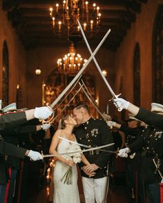 a bride and groom kiss as they hold swords in front of their heads at the end of an aisle