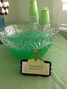 there is a glass bowl on the table with green cups in front of it and a name tag that says tia's