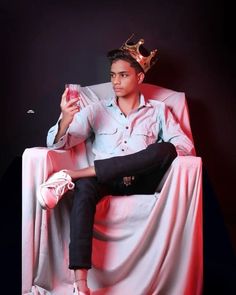 a man sitting in a chair with a crown on his head and holding a drink