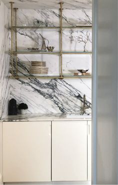 a kitchen with marble counter tops and white cupboards, gold shelves and brass accents