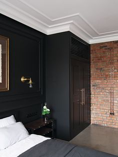 a bedroom with black walls and white linens on the bed, along with a brick wall