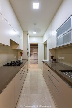 a long narrow kitchen with white cabinets and stainless steel counter tops, along with beige flooring