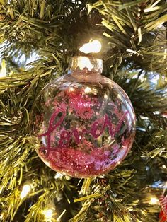 a glass ornament hanging from a christmas tree with the word joy written on it