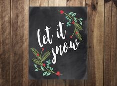 a chalkboard with the words let it snow written in white letters and decorated with evergreen leaves